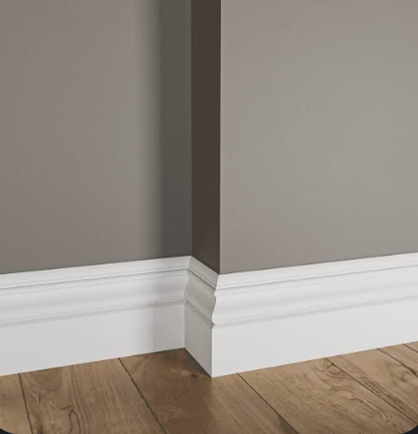White baseboard with a moulded profile meeting a wood plank floor at an inside corner