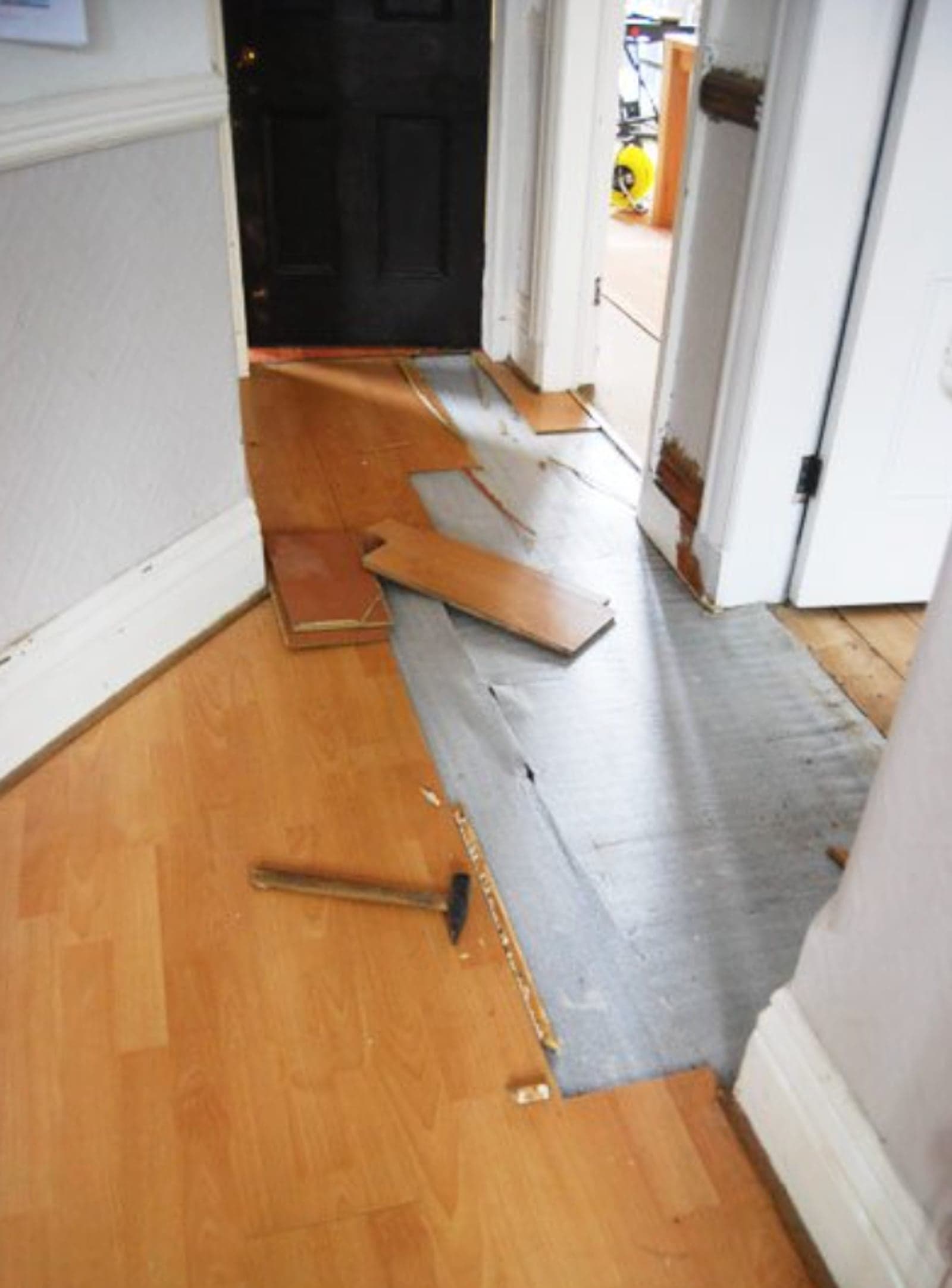 Old laminate plank flooring being lifted out of a hallway with the underlay exposed underneath