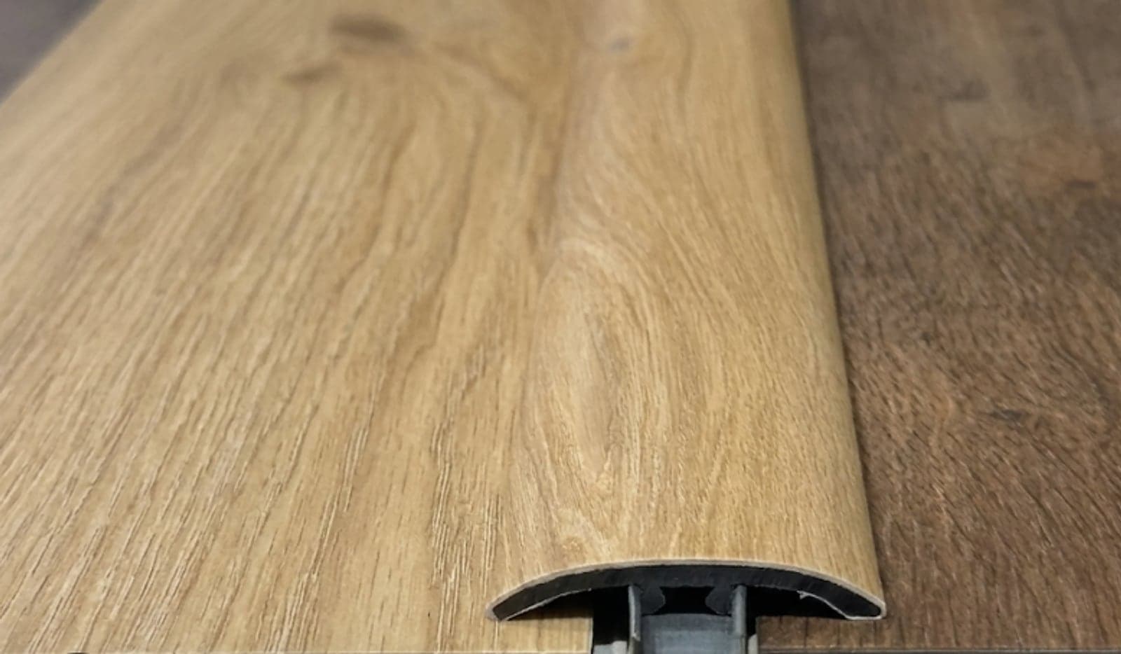 Close view of a wood-look transition strip and the track it clips into